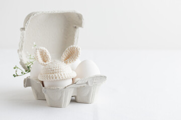 Easter egg in crochet hat with bunny ears in the eggbox on white
