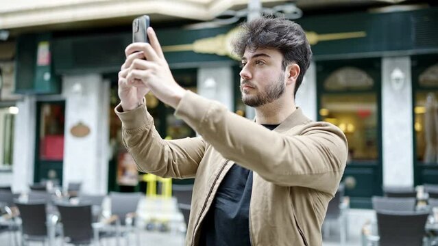 Young hispanic man recording video by smartphone at coffee shop terrace