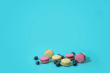 Colorful french macaroons and blueberries on a blue background