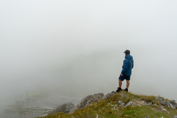 Fototapeta premium Man standing on top of mountain admiring landscape with fog