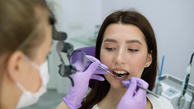 Female dentist examining young girl looking on the teeth with professional microscope in the surgery dental office