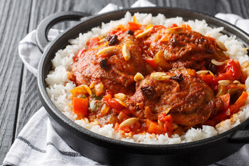 Country Captain chicken fried and then stewed with vegetables, raisins, almonds, tomato sauce and curry, served with rice in a pan on the table. Horizontal