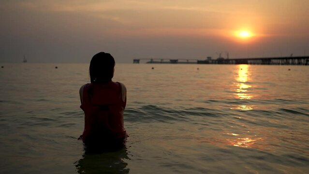 A woman is happily watching the sunset in the sea.