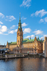 Fototapeta premium Schöner Blick auf das berühmte Hamburger Rathaus am Morgen bei blauem Himmel mit einzelnen Wolken vom Wasser aus, vertikal