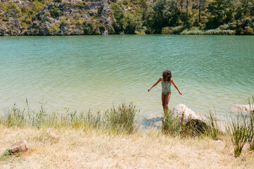 KId in swimwear in lake shore in beautiful landscape