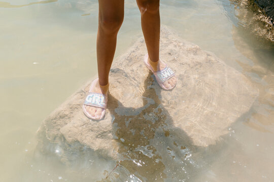 Child's legs standing on rock inside pond 