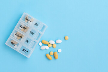 Top view of pill organizer with variety of pills and supplement. Weekly Pill container on blue...
