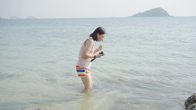Young Asian woman in walking and playing on tropical beach at summer sunset. Happy female enjoy and fun outdoor activity lifestyle on holiday travel vacation at the sea