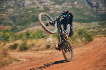 Cycling, training and person on a bicycle in the countryside for extreme sport, adrenaline and fun. Speed, action and cyclist on a dirt road for stunt, trick or fitness, freedom and balance in nature
