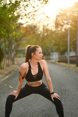 Fototapeta na wymiar Active fitness caucasian woman stretching and warming up before exercises in the park with bright sunlight on background