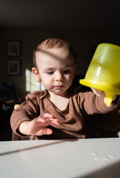 Toddler at the Table Plays with Sippy Cup of Milk