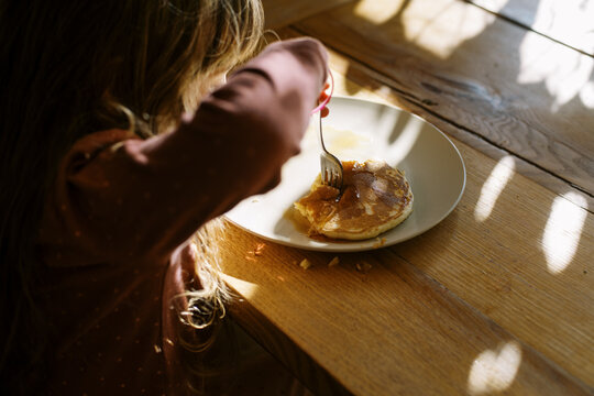 Little girl in pajamas eating pancake for breakfast at kitchen table