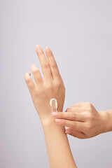 Hands of woman model applying cosmetic cream texture on her hand against a light background. Daily...