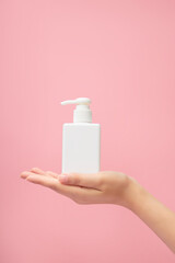 An elegant hand model with a pump bottle dispenser placed on over pink pastel background. Beauty cosmetic product for skin care concept. Mockup