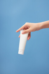 Beautiful female hand holding a tube in white color on blue background. Empty label for product...