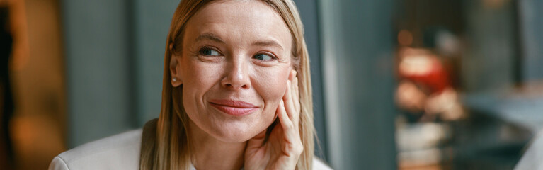 Close up portrait of attractive smiling businesswoman in jacket sitting in cafe and looking at side