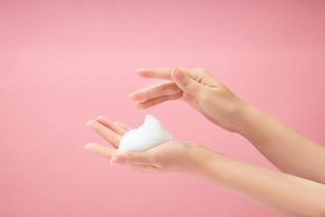 A beautiful woman hands with white foam mousse placed on over a pink background. Cosmetic product...