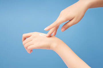 Woman's hand applying cream on the back of her other hand on a blue background. Advertisement scene...