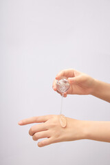 Front view of female hand pouring transparent essence on back of other hand on light background. Mockup scene for cosmetic product, daily skin care routine.
