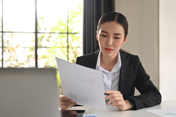 Serious asian woman financial analyst checking marketing report and using laptop at office desk. Business technology concept.
