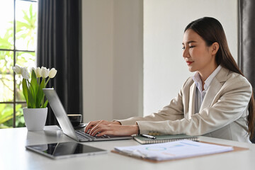 Attractive businesswoman using laptop on white office desk, web surfing information or checking email.