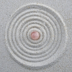 Fototapeta na wymiar rose quartz sphere in the middle of circles drawn in sand