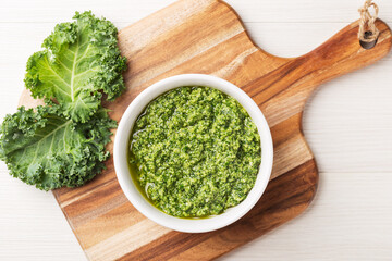 Top view on homemade pesto sauce with curly kale in a white bowl on a light wood background....