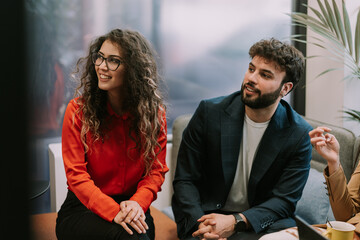 A front view photo of young curly haired businesswoman sitting next to her good looking boyfriend