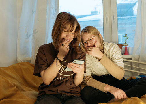 Two teenager girl friends sitting in a bedroom on a bed
