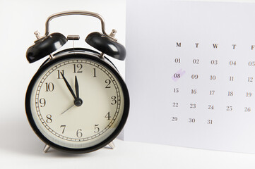 White calendar with marked date 8 March and black retro alarm clock on white background using as...