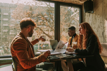 Redhead businesswoman showing sales charts to her young male manager. He is about to take a sip of...