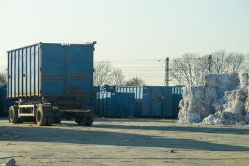 Heavy trailer parked in the recycling yard along plastic waste bales and blue metal containers.