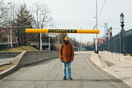 young tall man stands under a clearance bar in the middle of a road
