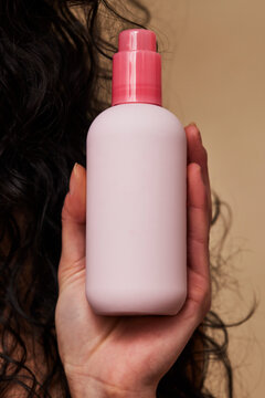 Woman's hand holding pink skincare bottle