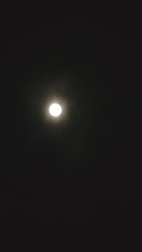A footage of a bright full moon illuminating the cloudy night sky. Vertical video.