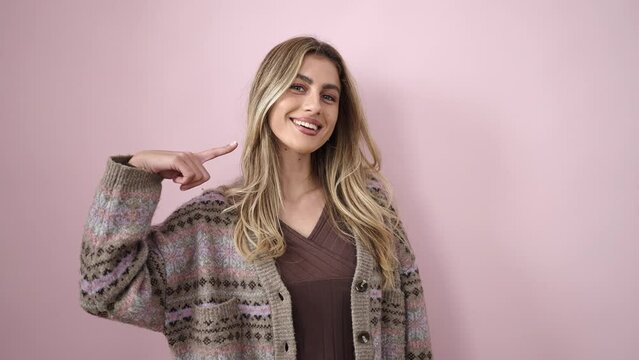 Young blonde woman smiling confident pointing to mouth with finger over isolated pink background