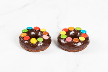 Obraz na płótnie Canvas Two Chocolate donuts with chocolate glaze and decorated with colored candy dragees. White background