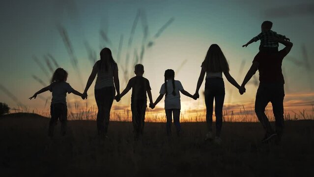 Happy big family.Silhouette of large group of people at sunset in park.People walk on green grass.Large family together holding hand walk through meadow in nature.Parents and children together in park