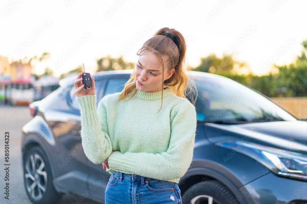 Wall mural Young pretty girl holding car keys at outdoors with sad expression