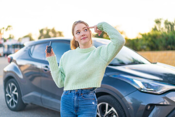 Young pretty girl holding car keys at outdoors having doubts and with confuse face expression