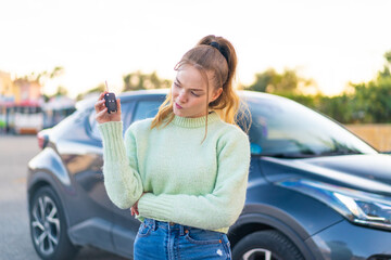 Young pretty girl holding car keys at outdoors with sad expression