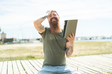Redhead man with beard holding a tablet at outdoors has realized something and intending the...