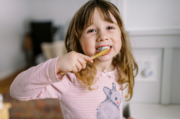 happy toddler girl in bathroom brushing her teeth by herself