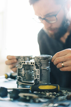 Millennial Man assembling carburetor on kitchen table in his home 