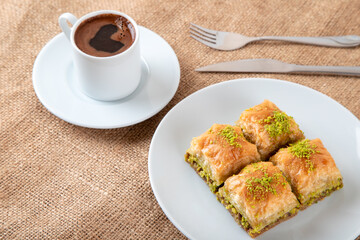 Pistachio baklava on a white plate with Turkish coffee.A plate of traditional baklava on burlap sack