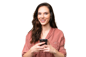 Young caucasian woman over isolated background looking at the camera and smiling while using the mobile