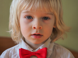 portrait of a child boy blond in a white shirt with a red bow tie