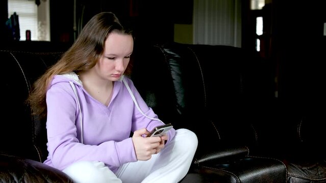 Smiling teenage girl relax, sit on couch at home using a mobile phone, chat with a friend, happy young woman on the couch, keep a smartphone in an online store or check mobile app or social networks