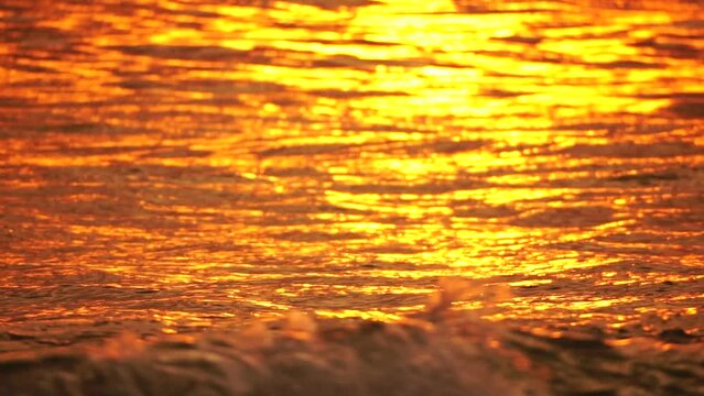 Blurred golden sea at sunset. The sun reflects and sparkles on the waves with bokeh, illuminating the golden sea. Holiday recreation concept. Abstract nautical summer ocean sunset nature background.