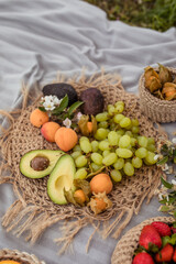 Naklejka na ściany i meble Summer picnic in nature with avocado peach and grapes on a straw plate